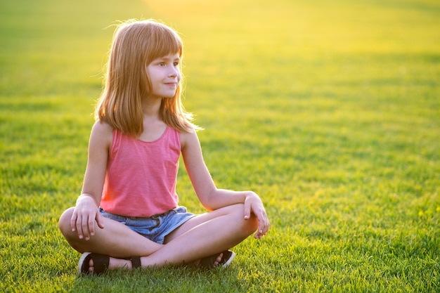 Giovane ragazza felice del bambino che riposa mentre è seduto sul prato di erba verde in una calda giornata estiva.