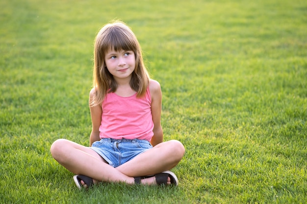 Giovane ragazza felice del bambino che riposa mentre è seduto sul prato di erba verde nelle calde giornate estive.