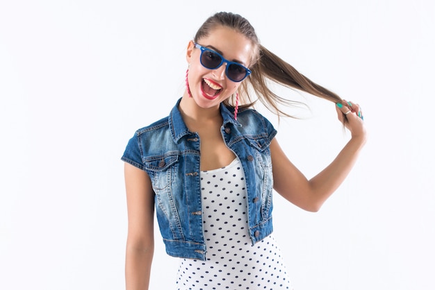 giovane ragazza felice ridendo, tenendo i capelli, imitando l'acconciatura della coda, indossando occhiali da sole e vestito alla moda.