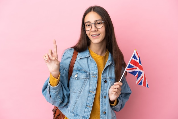 Giovane ragazza francese con una bandiera del Regno Unito isolata su sfondo rosa che mostra e alzando un dito in segno del meglio