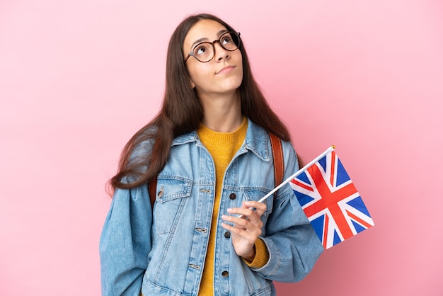 Giovane ragazza francese con una bandiera del Regno Unito isolata su sfondo rosa e alzando lo sguardo