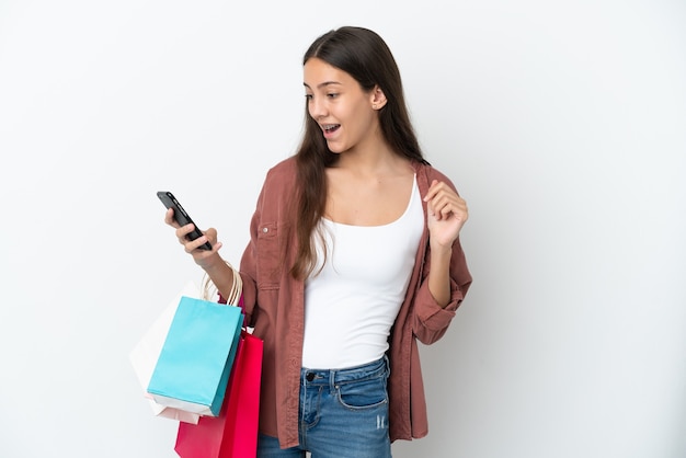 Giovane ragazza francese isolata su sfondo bianco tenendo le borse della spesa e scrivendo un messaggio con il cellulare a un amico