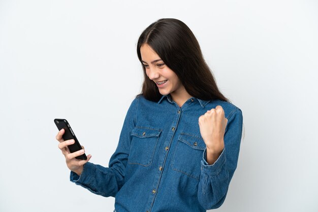 Giovane ragazza francese isolata su sfondo bianco utilizzando il telefono cellulare e facendo il gesto di vittoria