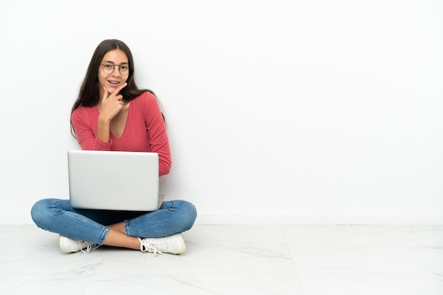 Giovane ragazza francese seduta per terra con il suo laptop sorridente