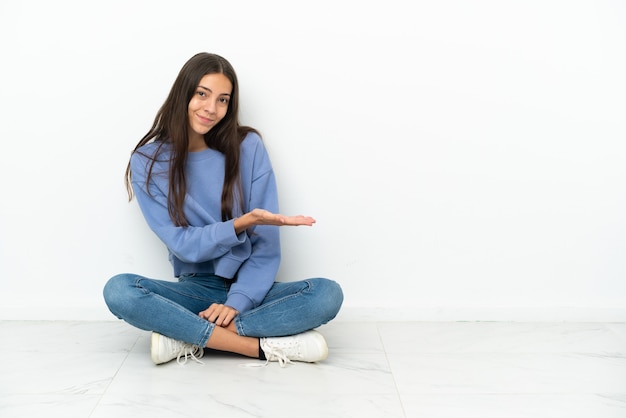 Giovane ragazza francese seduta sul pavimento che presenta un'idea mentre guarda sorridendo verso