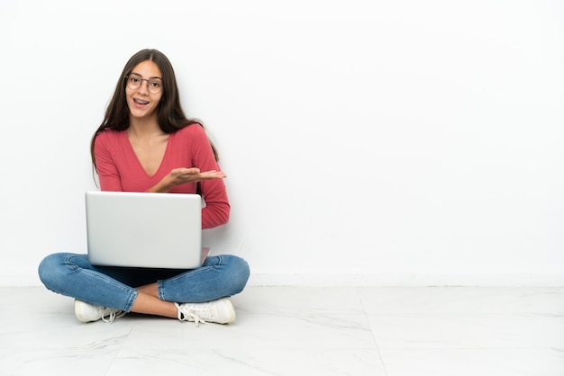 Giovane ragazza francese seduta sul pavimento con il suo laptop che presenta un'idea mentre guarda sorridendo verso