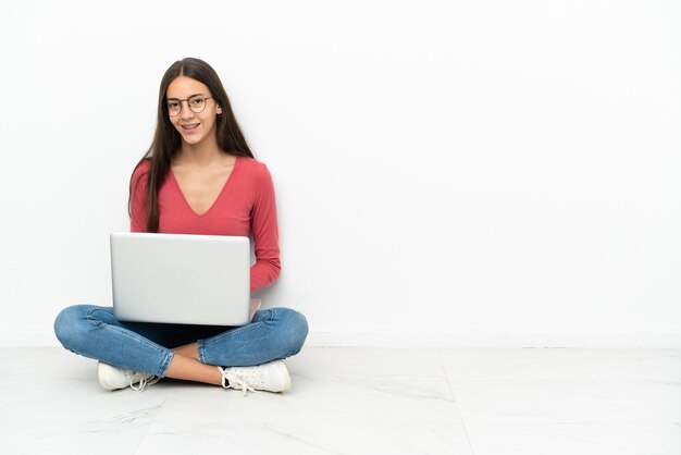 Giovane ragazza francese seduta sul pavimento con il suo laptop che ride