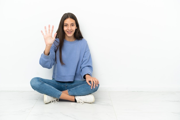 Giovane ragazza francese seduta sul pavimento contando cinque con le dita