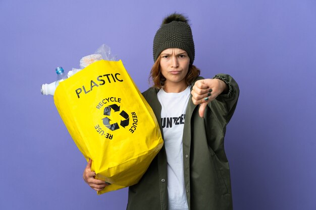 Giovane ragazza georgiana che tiene una borsa piena di bottiglie di plastica da riciclare che mostra il pollice verso il basso con espressione negativa