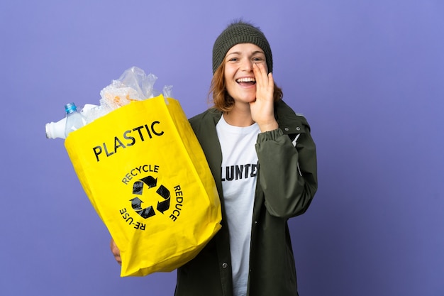 Giovane ragazza georgiana che tiene una borsa piena di bottiglie di plastica da riciclare gridando con la bocca spalancata