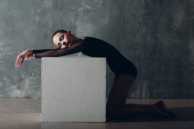 Giovane ragazza ginnasta professionista donna ginnastica ritmica rilassante con cubo bianco in studio.