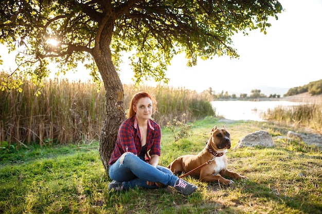 Giovane ragazza gioiosa che accarezza il loro cane indossando abbigliamento sportivo godendo il loro tempo e le vacanze nel parco soleggiato