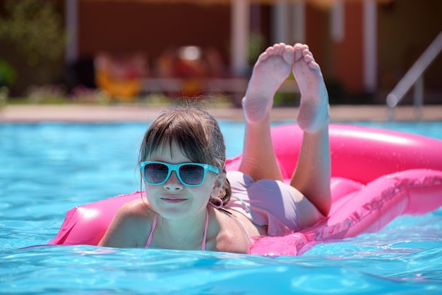 Giovane ragazza gioiosa del bambino che si diverte a nuotare sul materasso ad aria gonfiabile in piscina con acqua blu in una calda giornata estiva in vacanze tropicali Concetto di attività estive