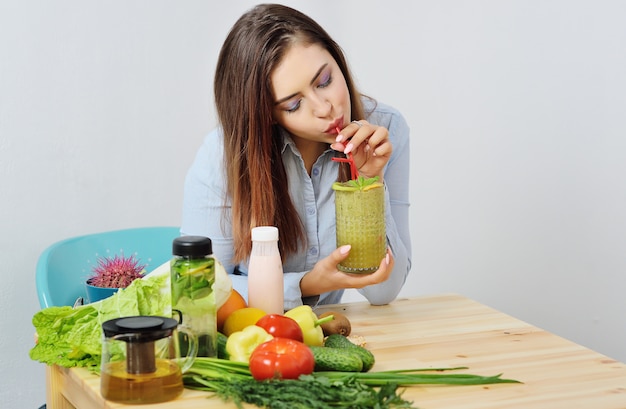 Giovane ragazza graziosa che tiene un grande bicchiere di frullati sulla superficie delle verdure.