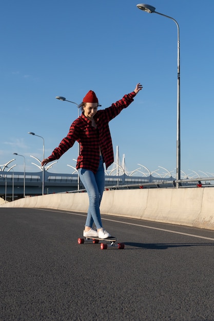 Giovane ragazza hipster che fa skateboard sulla strada della città felice gode di un giro in longboard giovanile e stile di vita urbano