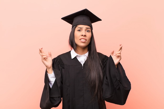 giovane ragazza in abito laurea incrocio le dita con ansia e sperando in buona fortuna