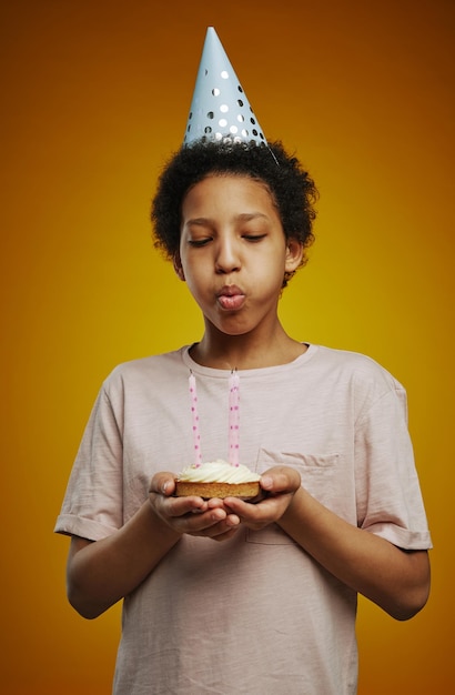 Giovane ragazza in cappello di compleanno che soffia le candeline su una piccola torta fatta in casa mentre si trova di fronte è venuto
