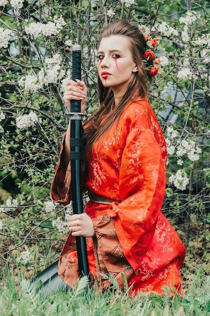 Giovane ragazza in kimano tradizionale in un giardino fiorito con katana spada giapponese samurai a immagine della donna guerriera