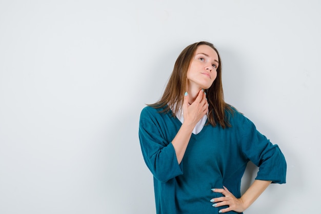 Giovane ragazza in maglione con scollo a V, camicia con mano sul collo e sguardo malinconico, vista frontale.