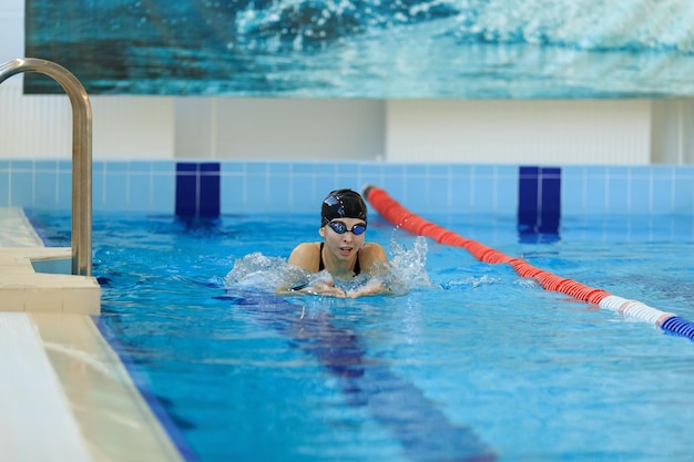 Giovane ragazza in occhiali e berretto da nuoto in stile colpo di farfalla nella piscina di acqua blu.