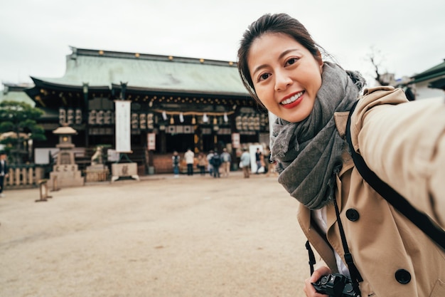 giovane ragazza in piedi nel terreno del tempio di tenmangu viso fotocamera sorridente. signora fotografa che si fa selfie con lo storico santuario giapponese a osaka in giappone. donna tourit prendendo autoritratto con lo shintoismo