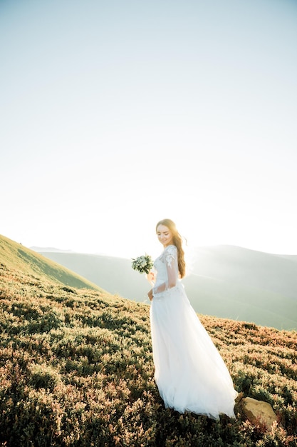giovane ragazza in un abito da sposa passeggiata in montagna all'alba al mattino