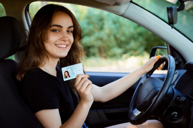 Giovane ragazza in un'auto moderna che mostra la patente di guida