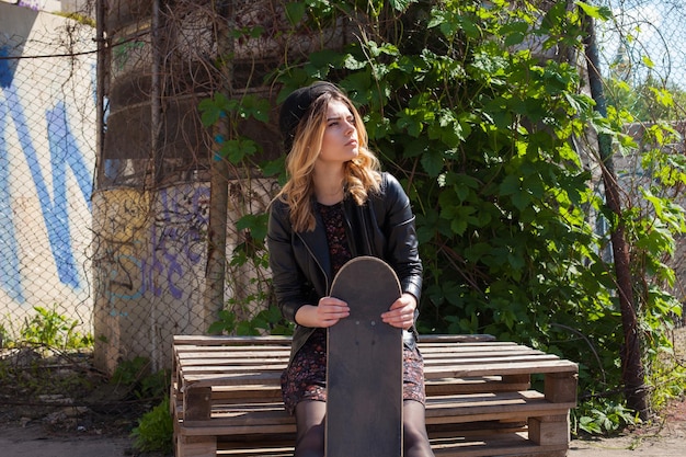 Giovane ragazza in un cappello seduto con lo skateboard e alzando lo sguardo