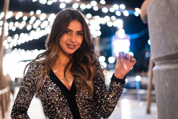 Giovane ragazza in un vestito alla moda con paillettes nelle luci di Natale della città