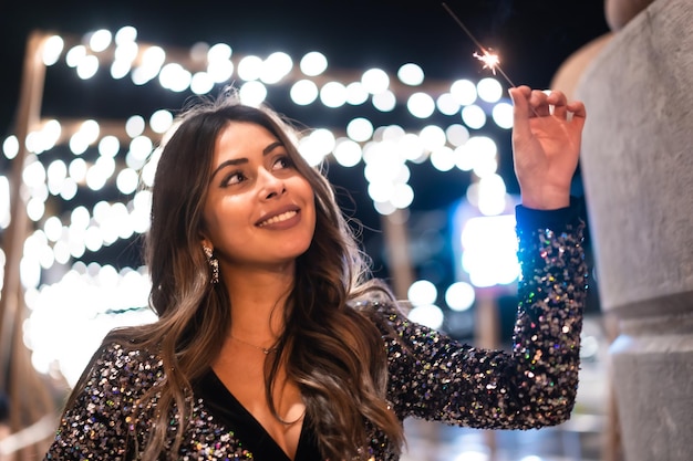 Giovane ragazza in un vestito alla moda con paillettes nelle luci di Natale della città