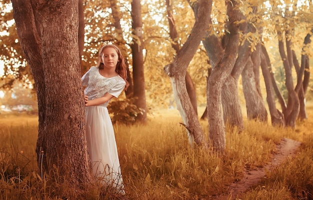 Giovane ragazza in un vestito bianco contro un albero in autunno