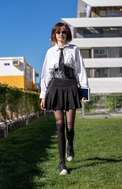 Giovane ragazza in uniforme che cammina sul prato davanti a un edificio, vista frontale, immagine verticale