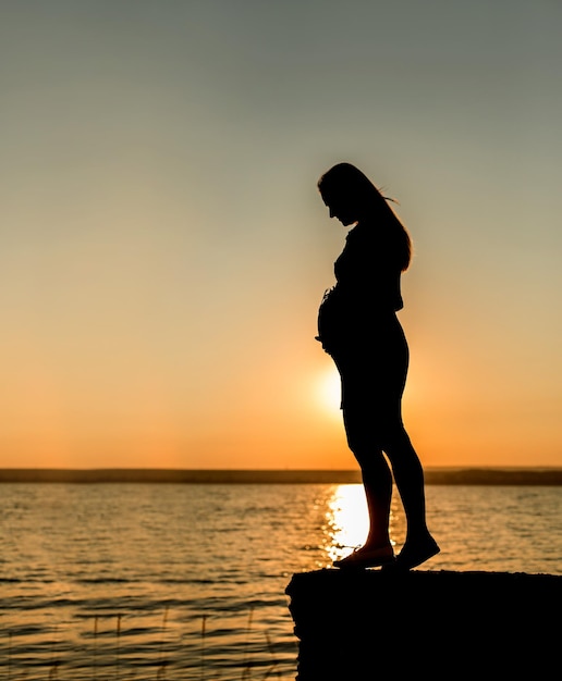 Giovane ragazza incinta sulla spiaggia silhouette