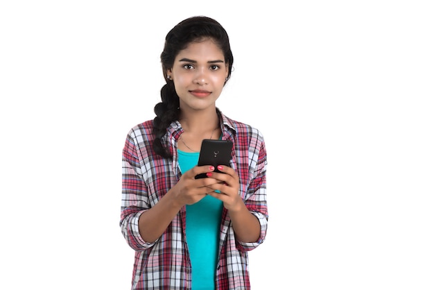 Giovane ragazza indiana che per mezzo di un telefono cellulare o di uno smartphone isolato su una parete bianca