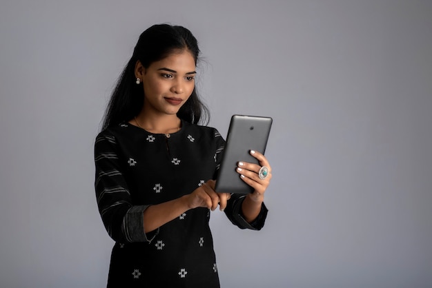 Giovane ragazza indiana utilizzando un telefono cellulare o uno smartphone su grigio