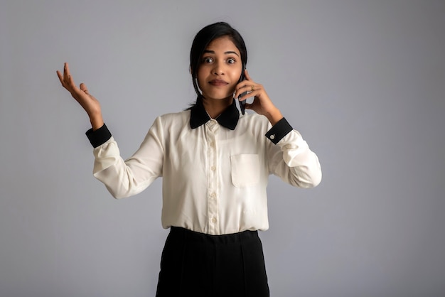 Giovane ragazza indiana utilizzando un telefono cellulare o uno smartphone sul muro grigio