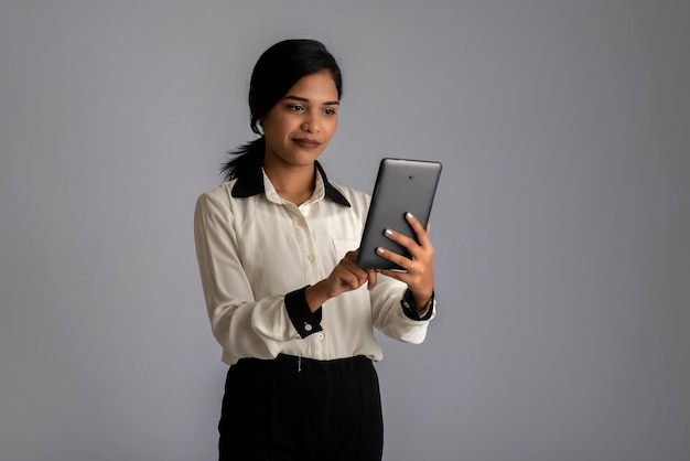 Giovane ragazza indiana utilizzando un telefono cellulare o uno smartphone sul muro grigio