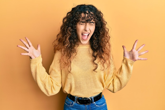 Giovane ragazza ispanica che indossa abiti casual che celebra pazza e pazza per il successo con le braccia alzate e gli occhi chiusi urlando il concetto di vincitore eccitato