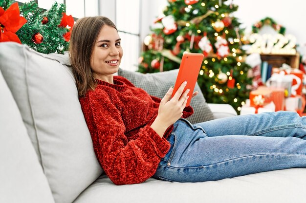 Giovane ragazza ispanica che usa il touchpad seduto sul divano accanto all'albero di Natale a casa.