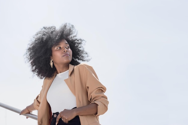 giovane ragazza latina ispanica nera con afro appoggiata su un corrimano fuori guardando a destra con copia spa