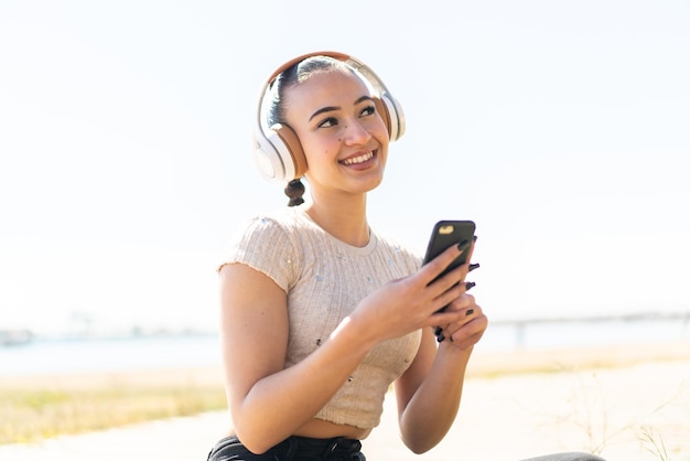 Giovane ragazza marocchina all'aperto ascoltando musica con un cellulare e pensando