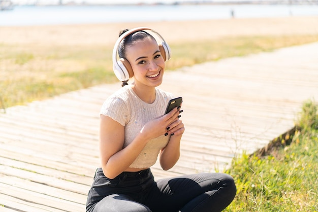 Giovane ragazza marocchina all'aperto che ascolta musica con un cellulare e guardando davanti