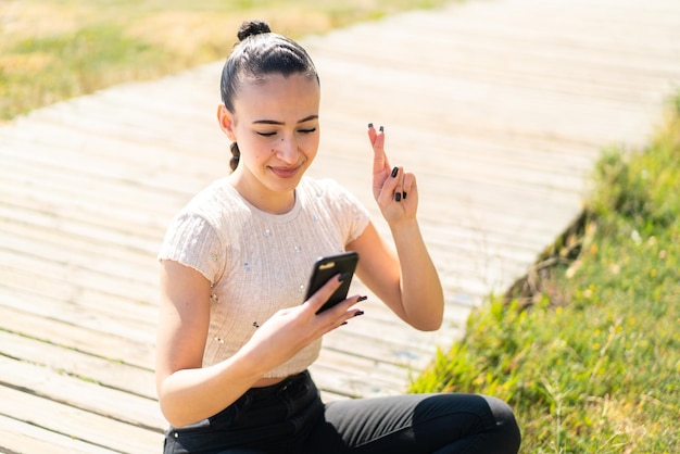 Giovane ragazza marocchina all'aperto utilizzando il telefono cellulare con le dita incrociate