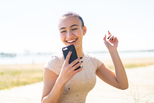 Giovane ragazza marocchina all'aperto utilizzando il telefono cellulare e cantando