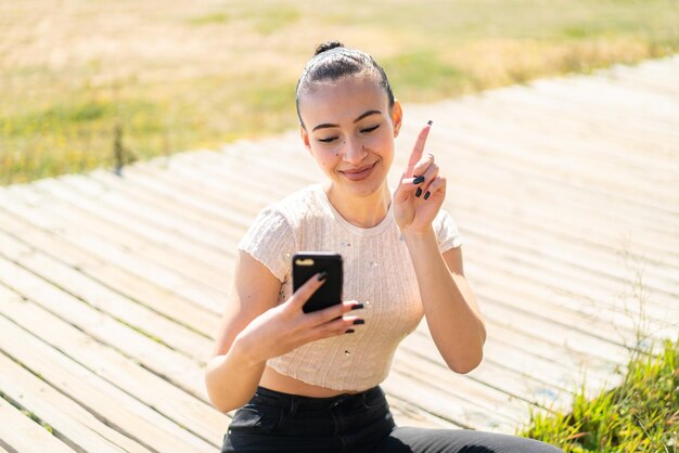 Giovane ragazza marocchina all'aperto utilizzando il telefono cellulare e il dito di sollevamento