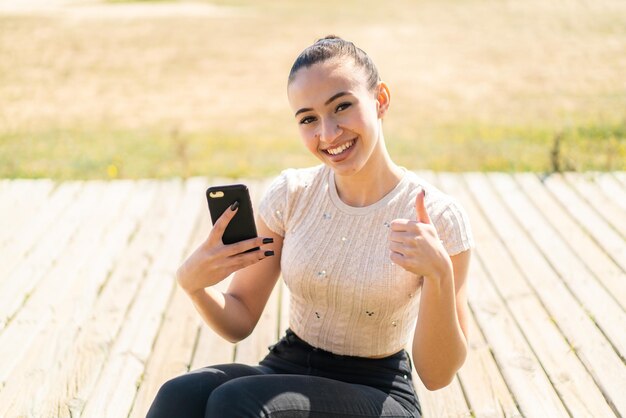 Giovane ragazza marocchina all'aperto utilizzando il telefono cellulare mentre si fa il pollice in alto