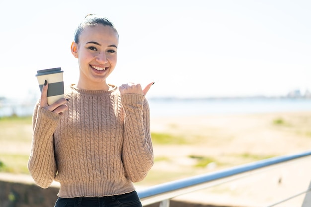 Giovane ragazza marocchina che tiene un caffè da asporto all'aperto che indica il lato per presentare un prodotto