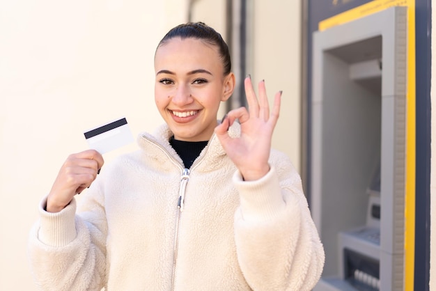 Giovane ragazza marocchina in possesso di una carta di credito all'aperto che mostra segno ok con le dita