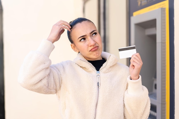 Giovane ragazza marocchina in possesso di una carta di credito all'aperto con dubbi e con espressione del viso confusa