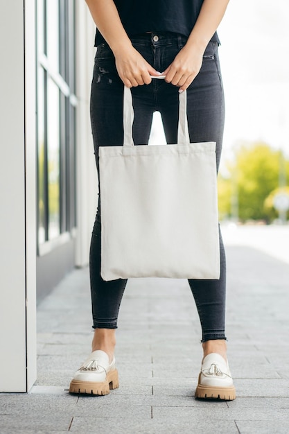 Giovane ragazza modello per strada che tiene in mano una borsa ecologica bianca